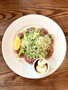 Lemon slice beef carpaccio, salad, parmesan and sauce, on a white plate