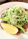 Lemon slice beef carpaccio, salad, parmesan and sauce, on a white plate