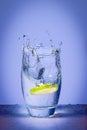 Lemon slice falls on mineral water and splashing water on blue background Royalty Free Stock Photo