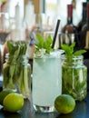 Lemonade drink in a glass with ice and mint leaves with a straw wine bottles on the background on a bar counter , two limes Royalty Free Stock Photo