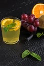 Lemonade drink of soda water, lemon and mint leaves in glass on the black background. Bunch of grapes and sliced citrus fruits Royalty Free Stock Photo