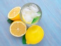 Lemonade in a glass, a lemon half, fresh leaves on the blue wood