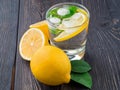 Lemonade in a glass, a lemon half, fresh leaves on dark brown wood table. A refreshing cold drink of water with ice, mint and Royalty Free Stock Photo