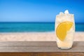 Lemonade with ice cubes and orange slice on table at beach, space for text