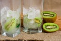 Lemonade from kiwi, water with ice, pieces of fruit in a glass cup. Summer detox breakfast on a wooden background.
