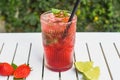 Lemonade strawberry and basil with ice on white wooden table against green leaves with copy space