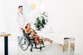 Length view of pediatrist in white coat and kid with teddy bear on wheelchair
