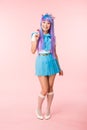 Length view of smiling asian otaku girl holding lollipop on pink Royalty Free Stock Photo