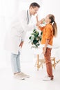 Length view of smiling pediatrist in white coat and child in clinic