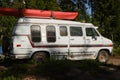 Leningrad Region, Russia - June 2022. Camping in a coniferous forest. American retro Dodge minivan with kayak on roof