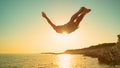 CLOSE UP: Beautiful golden sunbeams shine on fit man cliff diving at sunset. Royalty Free Stock Photo