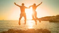 LENS FLARE: Golden sun rays shine on couple holding hands while diving into sea. Royalty Free Stock Photo