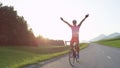 LENS FLARE: Happy sportsman riding his bicycle victoriously outstretching arms.