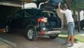 LENS FLARE: Man packing bags in car is about to close the trunk of black SUV.