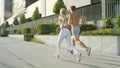 LENS FLARE: Man and woman with athletic physiques running in the sunny city. Royalty Free Stock Photo