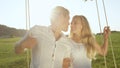 LENS FLARE PORTRAIT: Young adults cuddled up on romantic swing in sunlit nature.