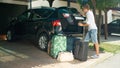 LENS FLARE: Smiling young man closes the back of his car after unpacking luggage