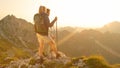 LENS FLARE: Unrecognizable cheerful hikers observe the golden sunset above Alps.