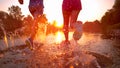 LENS FLARE: Unrecognizable couple jogging in shallow stream and towards sunset. Royalty Free Stock Photo