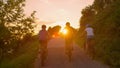 LENS FLARE: Unrecognizable cyclists pedal along the empty road at golden sunset. Royalty Free Stock Photo