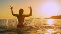 LENS FLARE Young woman sitting on a surfboard playfully splashes water at sunset Royalty Free Stock Photo