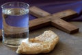 Lent season concept. Water, bread and cross on background of violet fabric Royalty Free Stock Photo