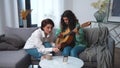 Lesbian couple. Girls studying playing guitar using smart phone with online teacher on sofa couch. Distance internet