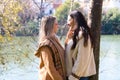 Lesbian couple leaning against a tree in a park with their hands clasped together. They look very much in love and happy as they