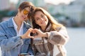 A lesbian couple is sitting on the embankment - they are showing heart shape with their fingers. Concept of equal rights Royalty Free Stock Photo