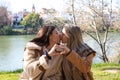 Lesbian couple sitting on a park bench. They look very much in love and happy while kissing and making a heart with their hands.