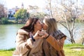 Lesbian couple sitting on a park bench. They look very much in love and happy while kissing and making a heart with their hands.