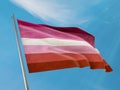 Lesbian flag on a pole waving. Lesbian realistic flag waving against clean blue sky.