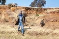 Lesotho, african young shepherd man in national woolen balaclava, dog and sheep, rocky stone slope Drakensberg mountains blue sky Royalty Free Stock Photo