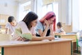 Lesson in class of high school students, female teacher sitting at desk with student