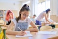 Lesson in class of teenage children, in front girl sitting at desk writing in notebook Royalty Free Stock Photo