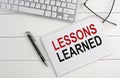 LESSONS LEARNED text on notebook with keyboard , pen glasses on white wooden background Royalty Free Stock Photo