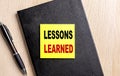 LESSONS LEARNED text on a sticky on black notebook with pen Royalty Free Stock Photo