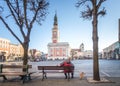 LESZNO, POLAND - FEBRUARY 16, 2019. An older man with a dog on a lead sitting on a bench in front of the Leszno Town Hall.