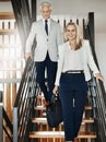 Let me take you on a tour. Portrait of two confident businesspeople walking down stairs together while talking inside a Royalty Free Stock Photo