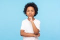 Let me think! Portrait of pensive clever curly preschooler in T-shirt standing with puzzled serious expression, child thinking Royalty Free Stock Photo