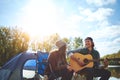 Let the music speak. a young man playing his girlfriend a song on his guitar while out camping.