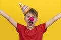 Let`s celebrate! April fools day. Cheerful child with red clown nose and festive hat on yellow background Royalty Free Stock Photo