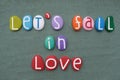 Let`s fall in love, creative message composed with multi colored stone letters over green sand