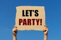 Let's party text on box paper held by 2 hands with isolated blue sky background.