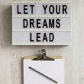 `Let your dreams lead` on a modern board, clipboard with blank sheet of paper on a white wooden surface, top view. Flat lay, Royalty Free Stock Photo