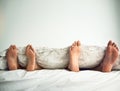 Lets cancel today and stay in bed. a couples feet poking out from under the bed sheets. Royalty Free Stock Photo