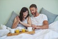 Lets dig in. a cheerful young couple sitting in bed while enjoying breakfast together during morning hours. Royalty Free Stock Photo