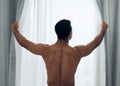 Lets get some light in here. a shirtless man opening the curtains at home.