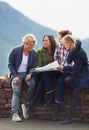 Lets move on to the next adventure. a group of friends sitting on a stone wall reading a map.