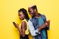 Lets see your secrets. Portrait of a young afro american couple standing back to back using mobile phones isolated over yellow bac Royalty Free Stock Photo